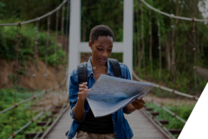 black woman walking on wood bridge through the woods reading a map