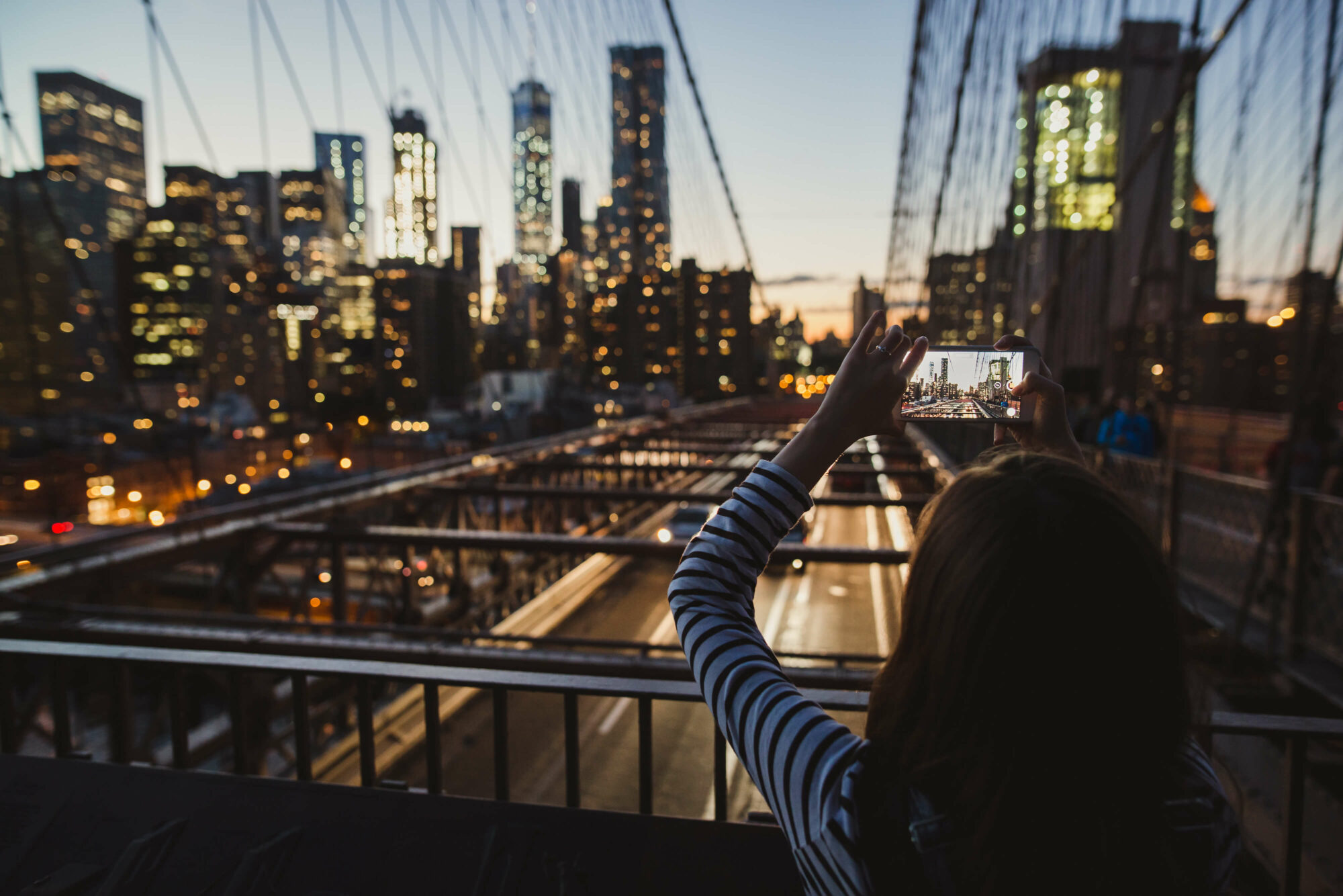 young woman taking a picture of large city on a bridge